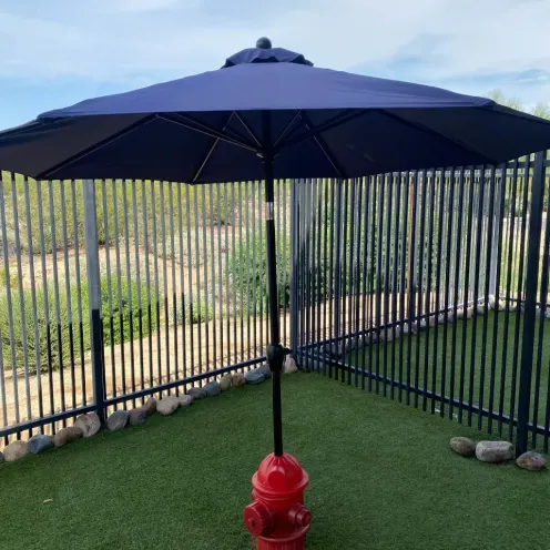 Patch of grass surrounded by fence and rocks and an umbrella being held by a red fire hydrant.